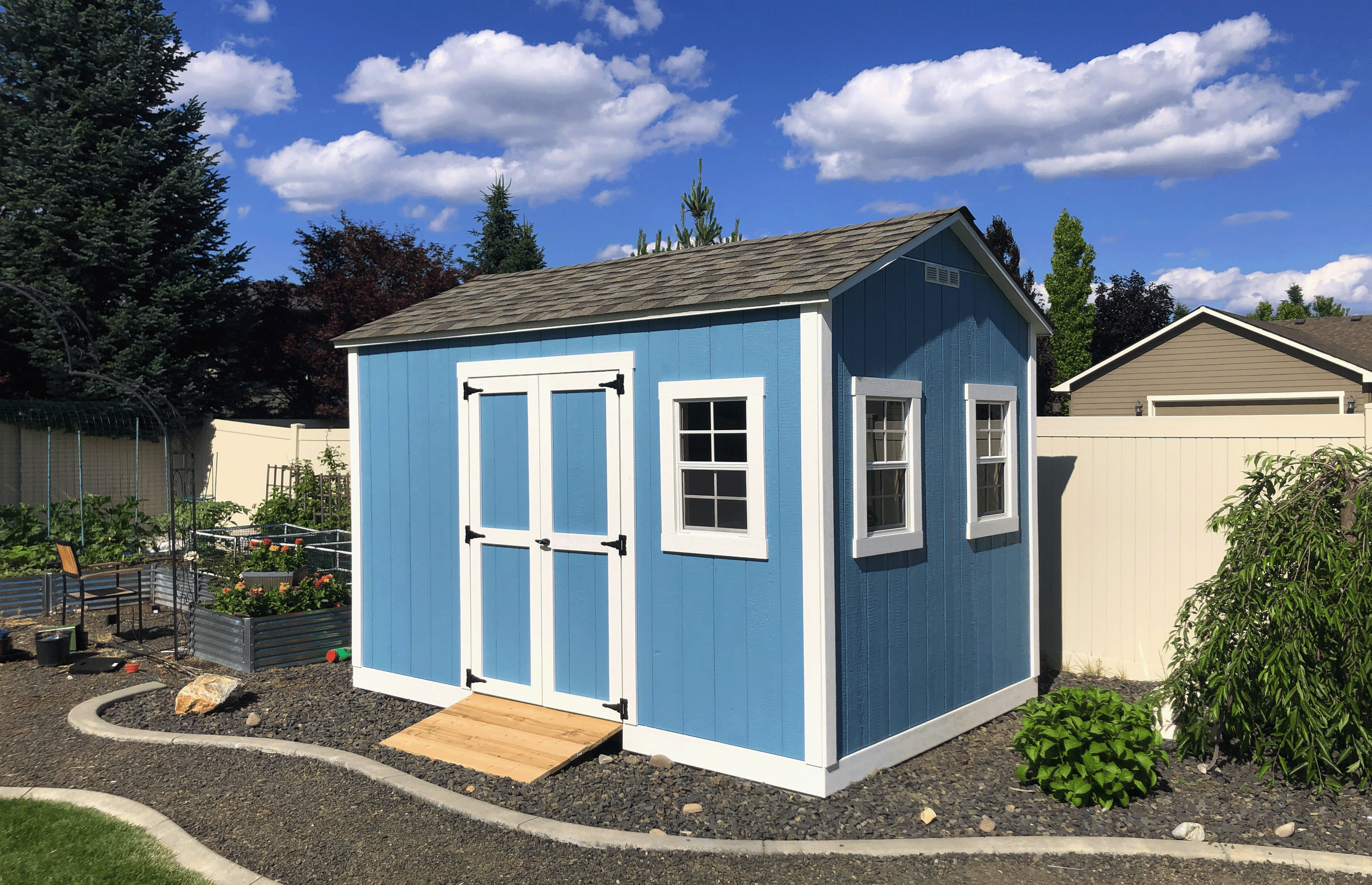 Blue garden shed with white trim in a backyard setting