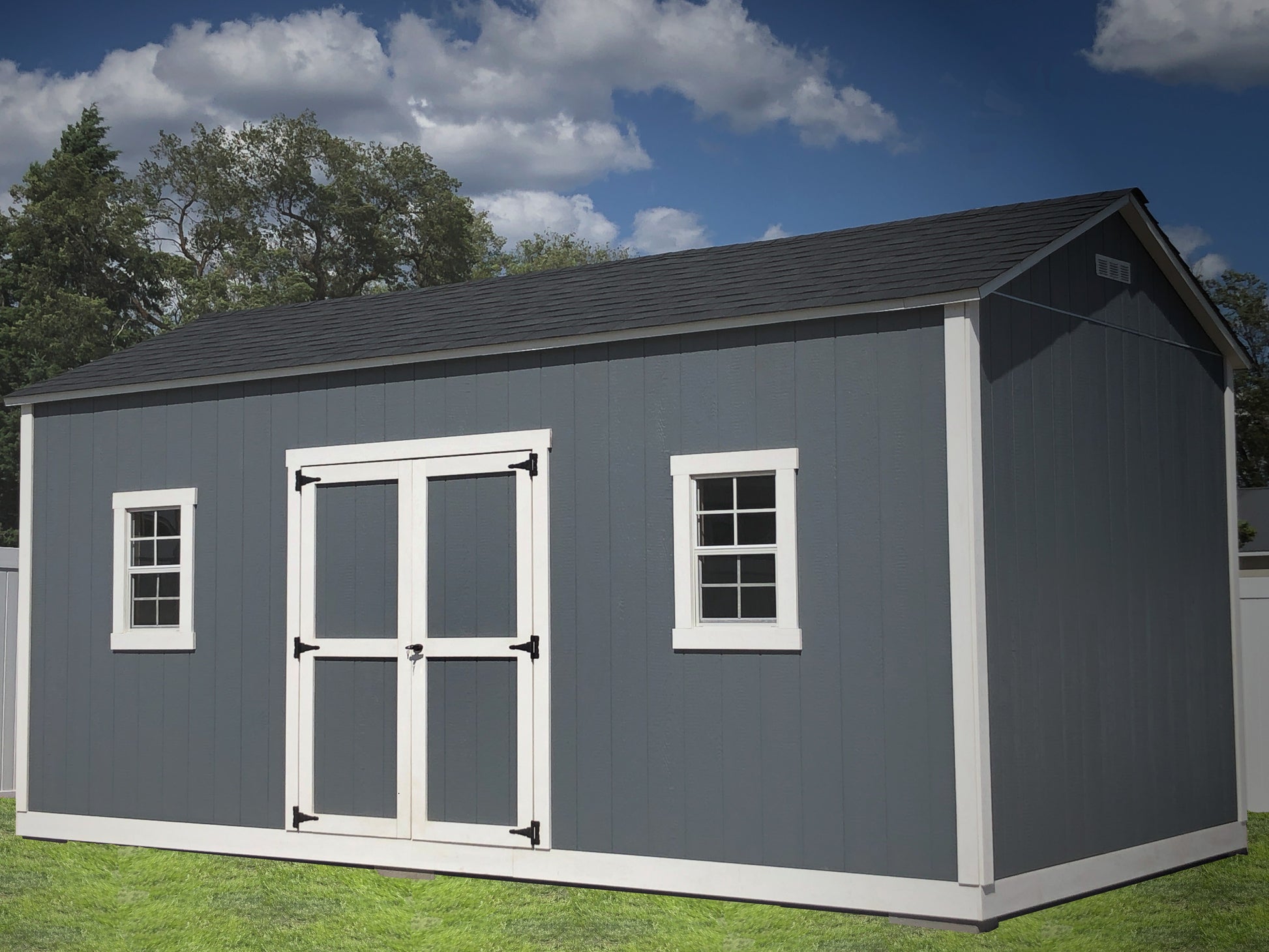 Gray storage shed with white trim on a grassy area with trees in the background