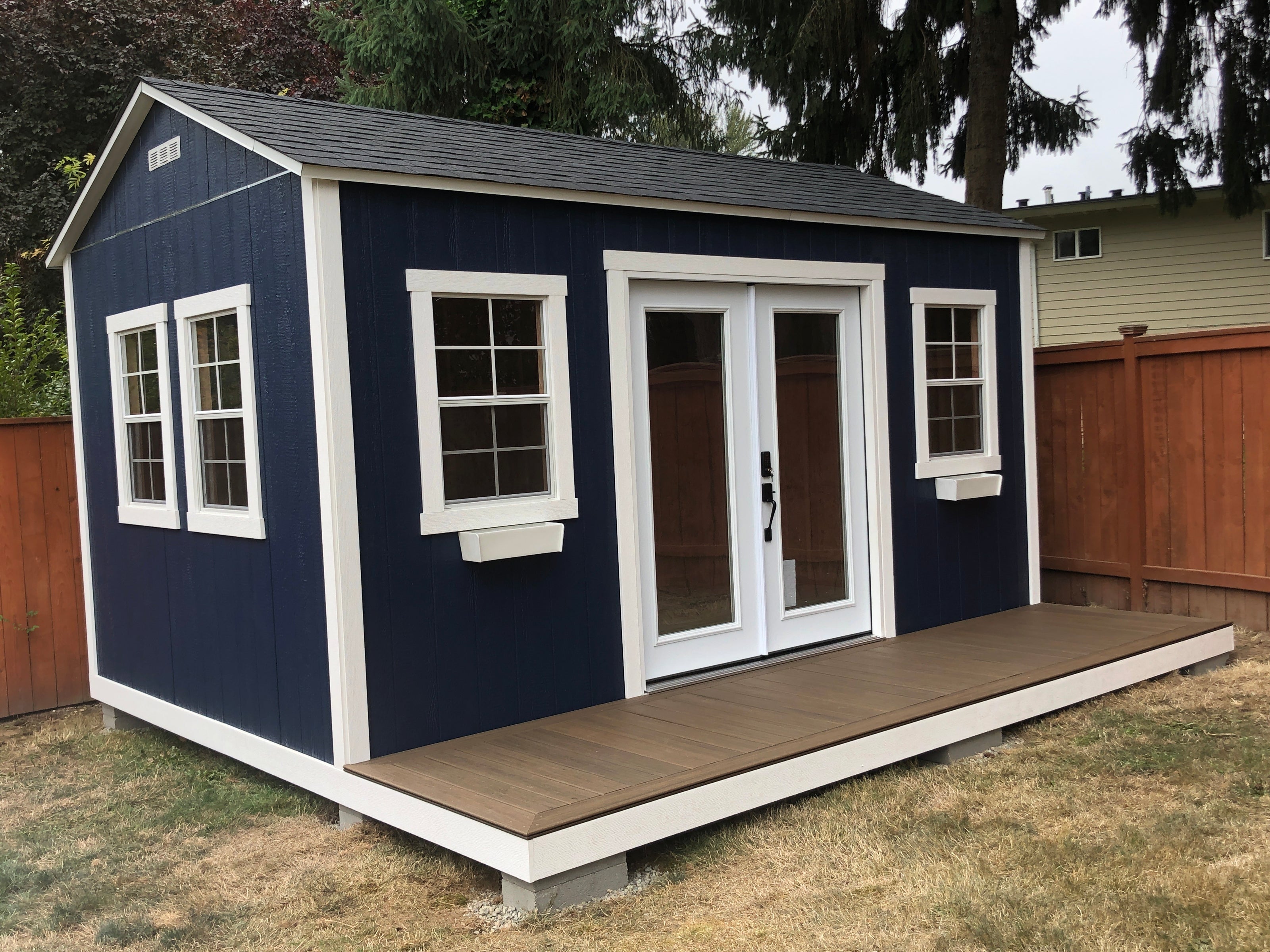 Blue shed with a wooden deck in a backyard setting